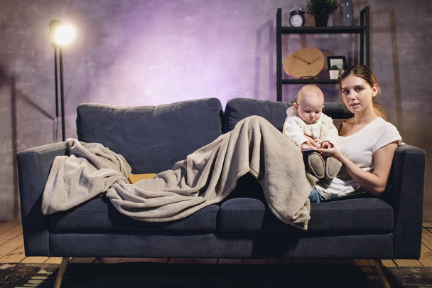 Nuori tyttö, jolla on lapsi katsomassa televisiota. Äiti ja vauva makaavat sohvalla. Kodikas huone
 - Valokuva, kuva