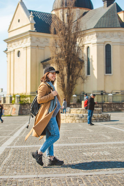 young pretty fashionable woman walking in brown coat by city street - Zdjęcie, obraz