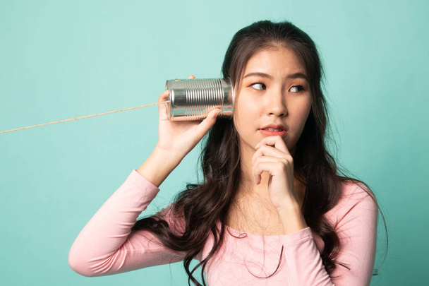 Joven asiática mujer audiencia con lata puede teléfono y pensando en cyan fondo
 - Foto, Imagen