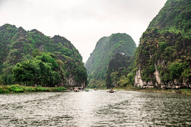 Tam Coc National Park - Tourists traveling in boats along the Ngo Dong River at Ninh Binh Province, Trang An landscape complex, Vietnam - Landscape formed by karst towers and rice fields - Foto, Imagen