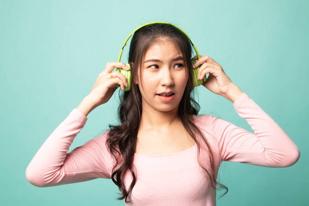 Too loud.  portrait of  young asian woman  holding  headphones and making unhappy face on cyan background - Valokuva, kuva