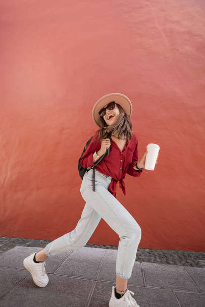 Портрет стильной женщины с чашкой кофе на фоне красной стены
 - Фото, изображение