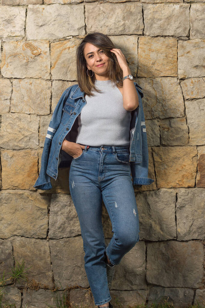 Pretty latin single woman portrait outdoors with a stone wall of background - Фото, изображение