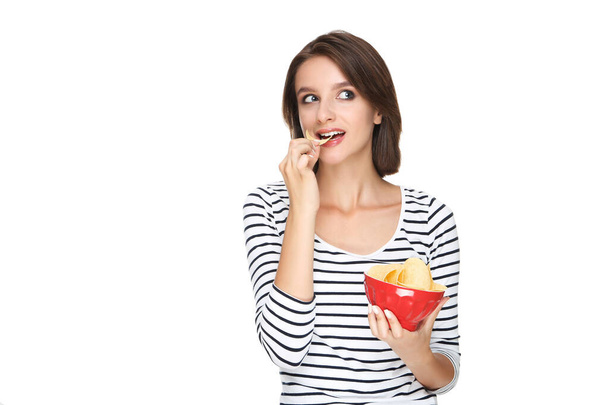 Krásná mladá žena jíst a držet bramborové lupínky v misce na bílém pozadí - Fotografie, Obrázek
