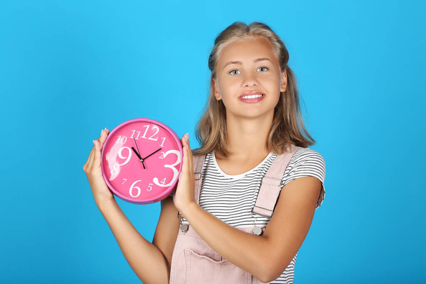 Young girl holding round clock on blue background - Valokuva, kuva