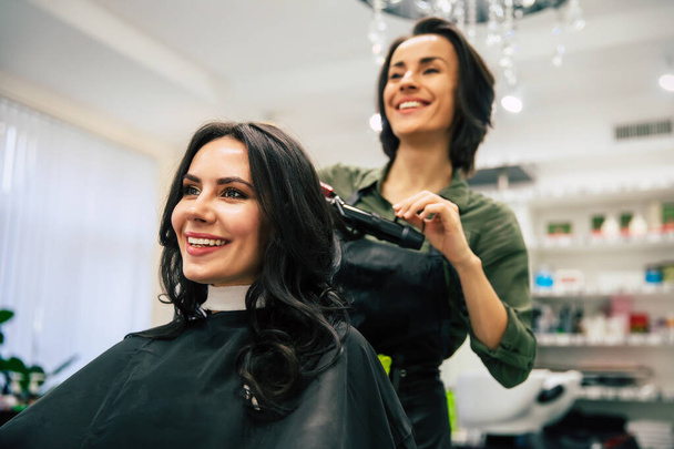 Peluquería femenina sonriendo, haciendo peinado a la mujer joven en el salón de belleza
 - Foto, imagen