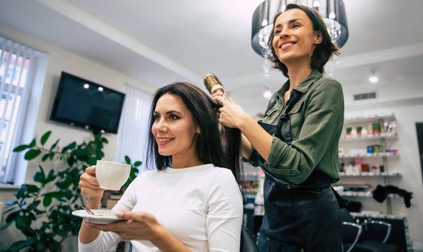 Female hairdresser smiling, making hairstyle to young woman in beauty salon - Foto, immagini