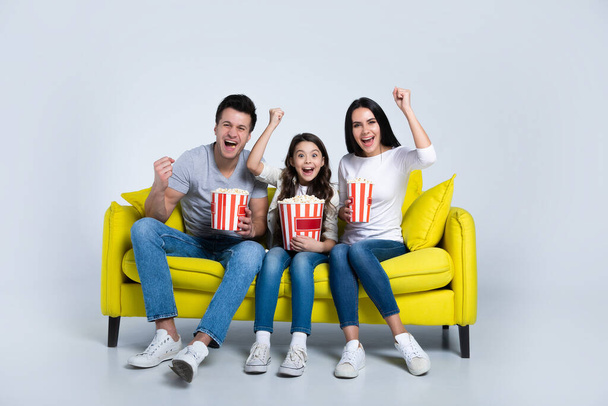 Happy young family watching tv at home with popcorn sitting on yellow sofa - Foto, Imagem