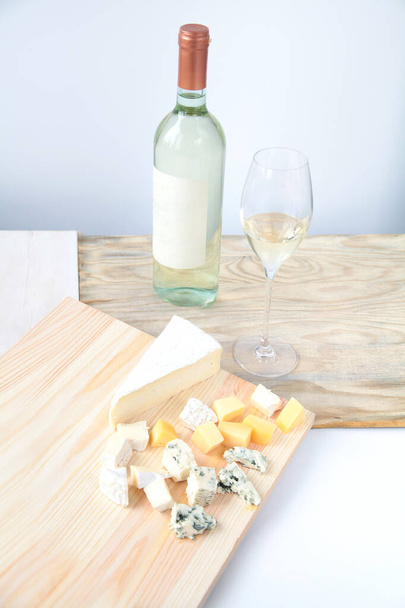 Fles witte wijn en wijnglazen, kaas op een houten ondergrond - Foto, afbeelding