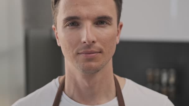 Close-up view of a young man cook is smiling to the camera in the kitchen - Filmagem, Vídeo