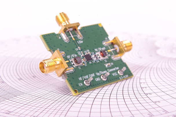 PCB de placa de circuito impreso mezclador de radiofrecuencia delante del gráfico Smith para cálculos de microondas y RF
 - Foto, Imagen