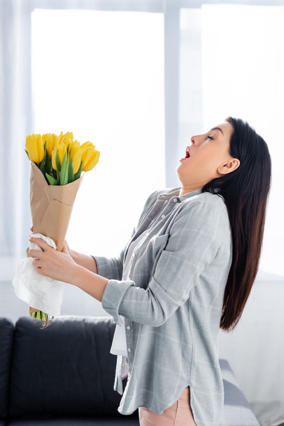 kichająca kobieta z alergią na pyłki i zamkniętymi oczami trzymająca tulipany  - Zdjęcie, obraz