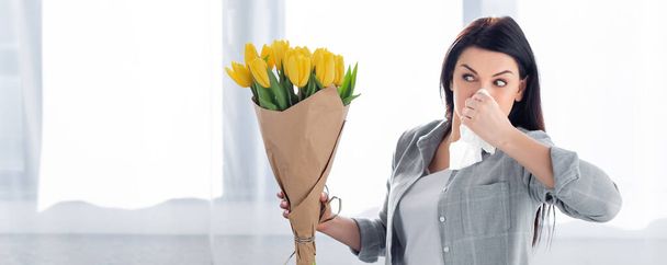tiro panorámico de mujer estornuda con alergia al polen mirando tulipanes
  - Foto, Imagen