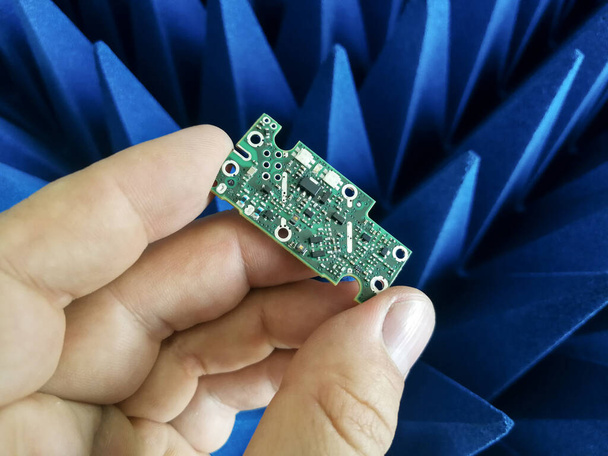 Πλακέτα τυπωμένου κυκλώματος χειρός ηλεκτρολόγου μηχανικού μπροστά από απορροφητές ραδιοσυχνοτήτων - Φωτογραφία, εικόνα