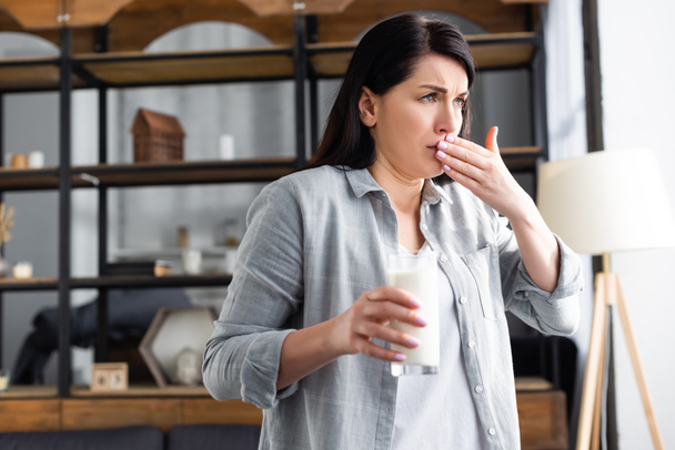 vrouw met lactose-intolerantie die een glas melk vasthoudt en de mond bedekt  - Foto, afbeelding