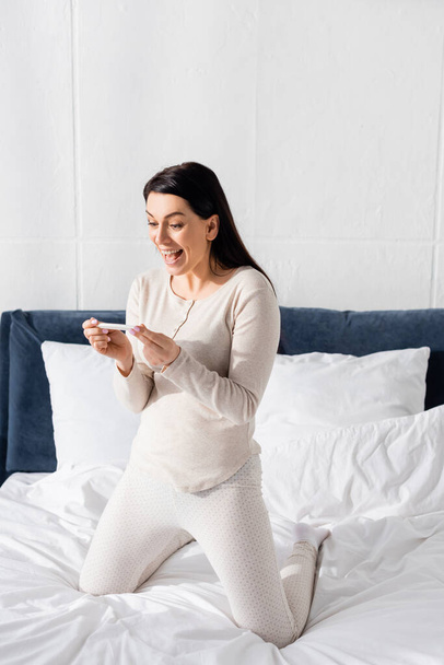 excited woman holding pregnancy test in bedroom  - Foto, Imagen