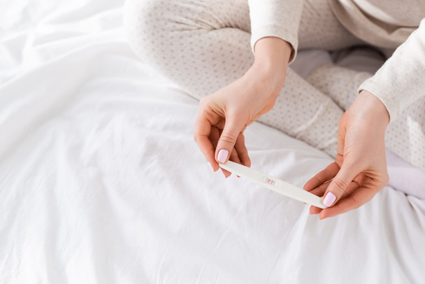 cropped view of woman holding pregnancy test in bedroom  - Φωτογραφία, εικόνα