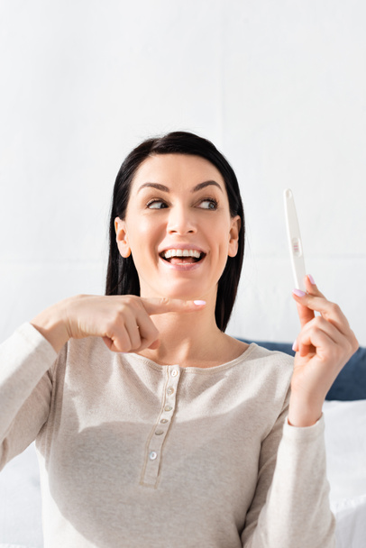 Glückliche Frau zeigt mit Finger auf Schwangerschaftstest  - Foto, Bild