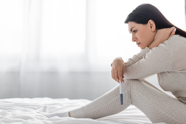 visão lateral da mulher triste segurando teste de gravidez com resultado negativo
  - Foto, Imagem