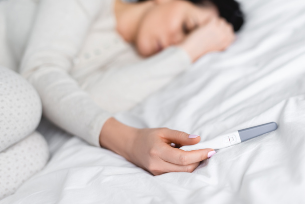 selective focus of depressed woman lying on bed and holding pregnancy test with negative result  - 写真・画像