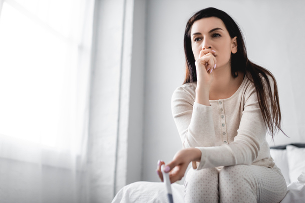 mujer deprimida sentada en la cama y sosteniendo la prueba de embarazo con resultado negativo
  - Foto, imagen