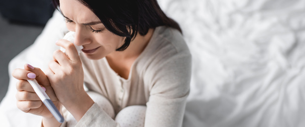 panoramisch schot van overstuur vrouw huilen en houden zwangerschapstest  - Foto, afbeelding