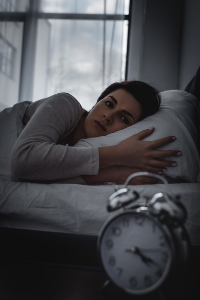 enfoque selectivo de la mujer despierta mirando el reloj despertador en la mesita de noche
  - Foto, Imagen