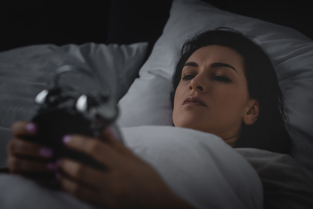 selective focus of awake woman looking at alarm clock  - Photo, Image