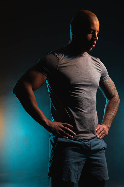 Young attractive sporty man standing with hands on the waist and looking down - Photo, image