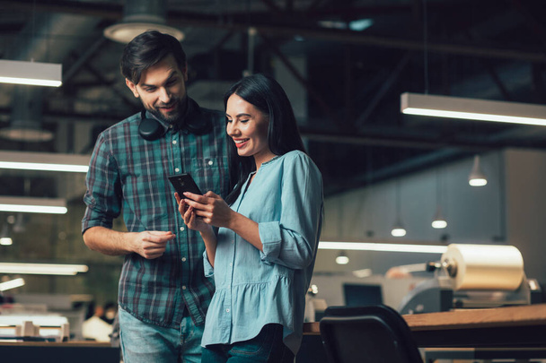 Friendly young man and woman in the office looking at the smartphone screen - Foto, Imagen