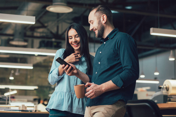 Uvolněný muž a žena se usmívají při pohledu na obrazovku smartphonu v práci - Fotografie, Obrázek
