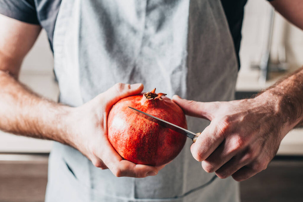 A man with strong hands cuts a pomegranate with a knife - close-up - Foto, imagen