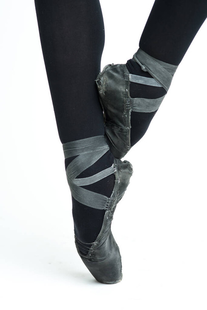 Em um fundo branco, pernas de bailarina femininas em sapatos velhos, desgastados e pretos Pointe. Chinelos tradicionais para ballet clássico
. - Foto, Imagem