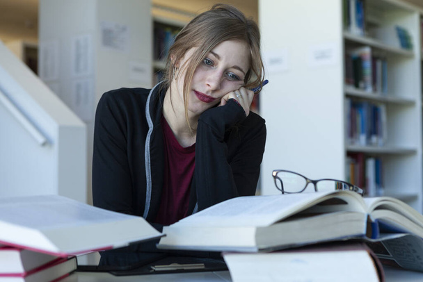 молодая женщина учится в библиотеке, скучно или насыщен и обеспокоен
 - Фото, изображение