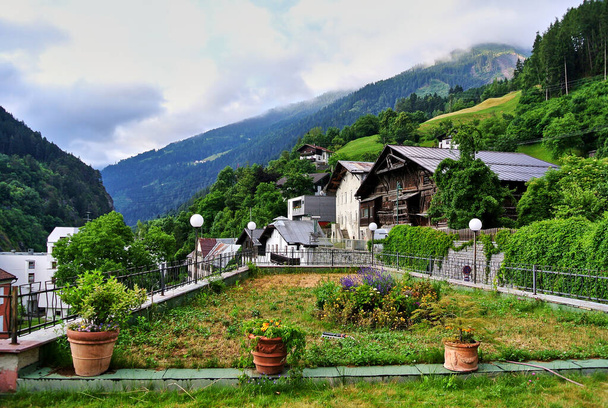 Landeck, Austria - Case in una piccola città, tra verdi montagne alpine ricoperte di foresta, vasi di fiori in primo piano, nuvole grigie nel cielo, nel pomeriggio estivo
. - Foto, immagini