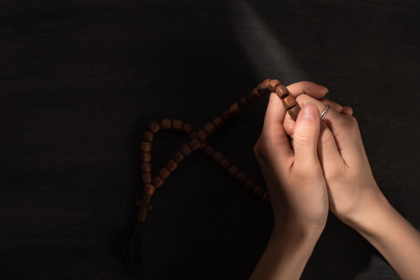 περικοπή άποψη της γυναίκας προσεύχεται με κομπολόι σε σκούρο φόντο - Φωτογραφία, εικόνα