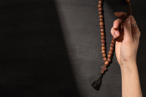 bijgesneden weergave van de vrouw bidden met rozenkrans op donkere achtergrond - Foto, afbeelding