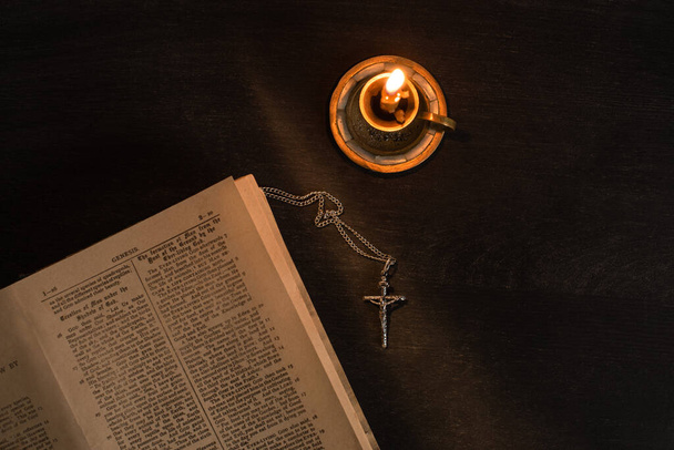 KYIV, UKRAINE - JANUARY 17, 2020: top view of open holy bible with cross and candle on dark background - Foto, imagen