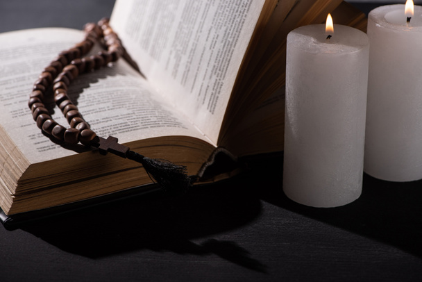 Sacra Bibbia con rosario su sfondo nero scuro con candele accese
 - Foto, immagini