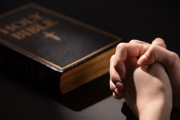 vista cortada da mulher orando perto da Bíblia sagrada no escuro
 - Foto, Imagem