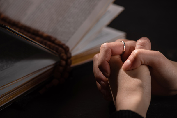 περικοπή άποψη της γυναίκας προσεύχεται κοντά Αγία Γραφή με κομπολόι στο σκοτάδι - Φωτογραφία, εικόνα