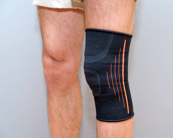 black elastic bandage on an injured knee on a light background - Foto, imagen