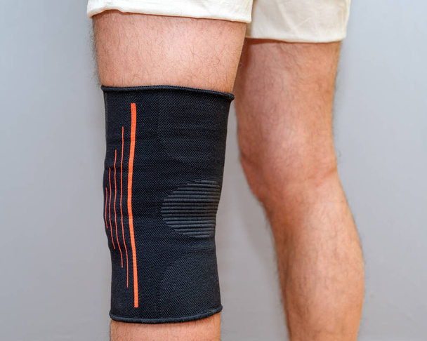 black elastic bandage on an injured knee on a light background - Fotoğraf, Görsel