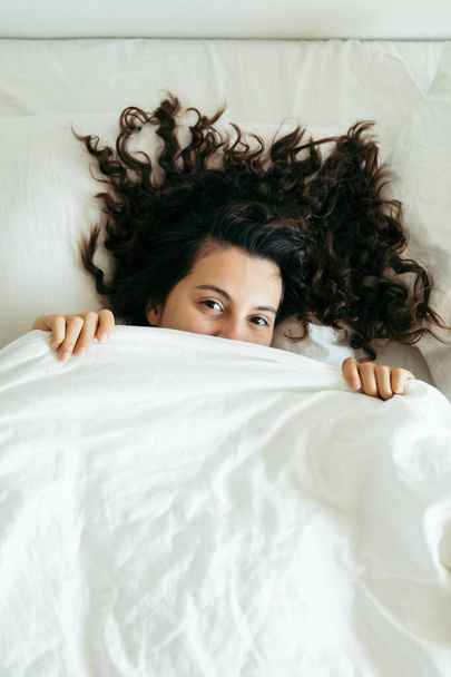 mujer divirtiéndose en cama ocultándose después de manta
 - Foto, imagen