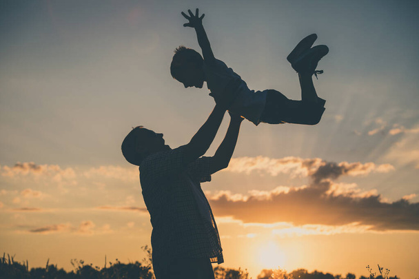 Father and son playing in the park at the sunset time. People having fun on the field. Concept of friendly family and of summer vacation. - Foto, imagen