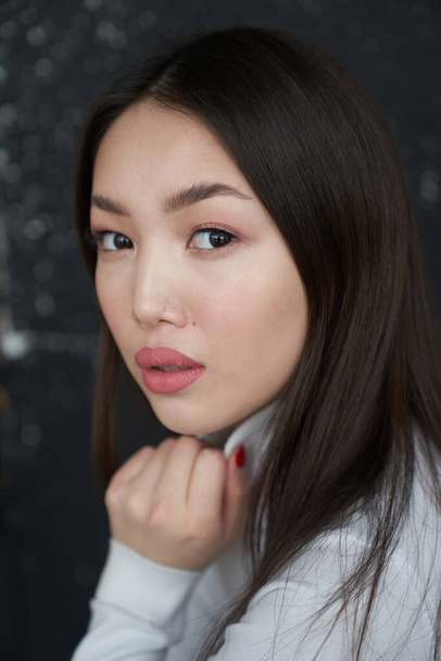 Portrait of a young Asian girl holding her hands to her face, looking directly at the camera. She's wearing a light turtleneck. The concept of skin care and hair                                       - Foto, Imagem