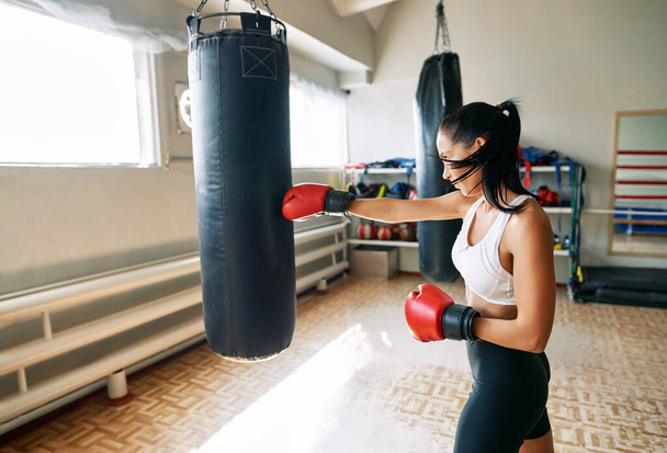 Female boxer hitting a huge punching bag at fitness gym. Woman practicing her punches at a boxing studio                  - Фото, зображення
