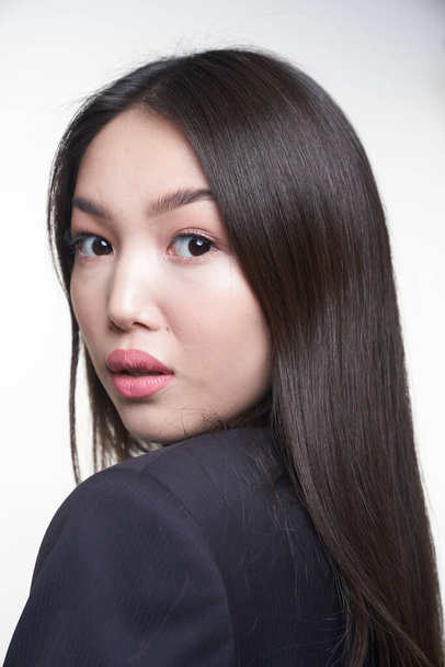 Retrato de uma jovem bela menina asiática olhando por cima do ombro, diretamente para a câmera, vestindo uma jaqueta azul. O conceito de cuidado de pele e cabelo
                                  - Foto, Imagem