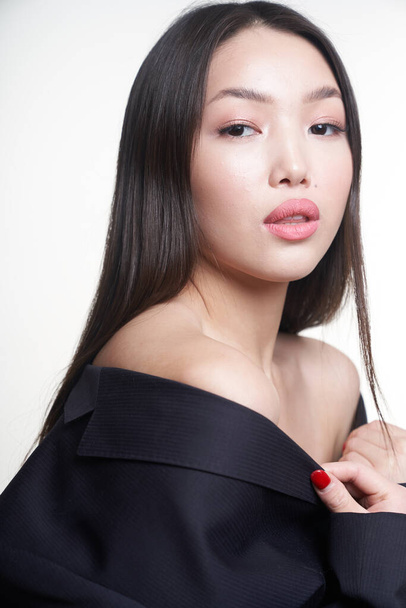  Portrait of a young beautiful Asian girl looking directly at the camera, shoulders open, hands pressed to her chest. The concept of skin care facial, makeup                                                     - Foto, afbeelding