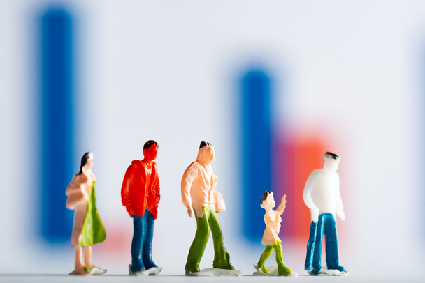 Selective focus of row of people figures on white surface with graphs at background, concept of equality - Foto, Imagen